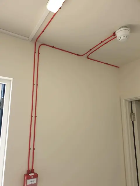 Red fire alarm cables run neatly to a ceiling detector and call point